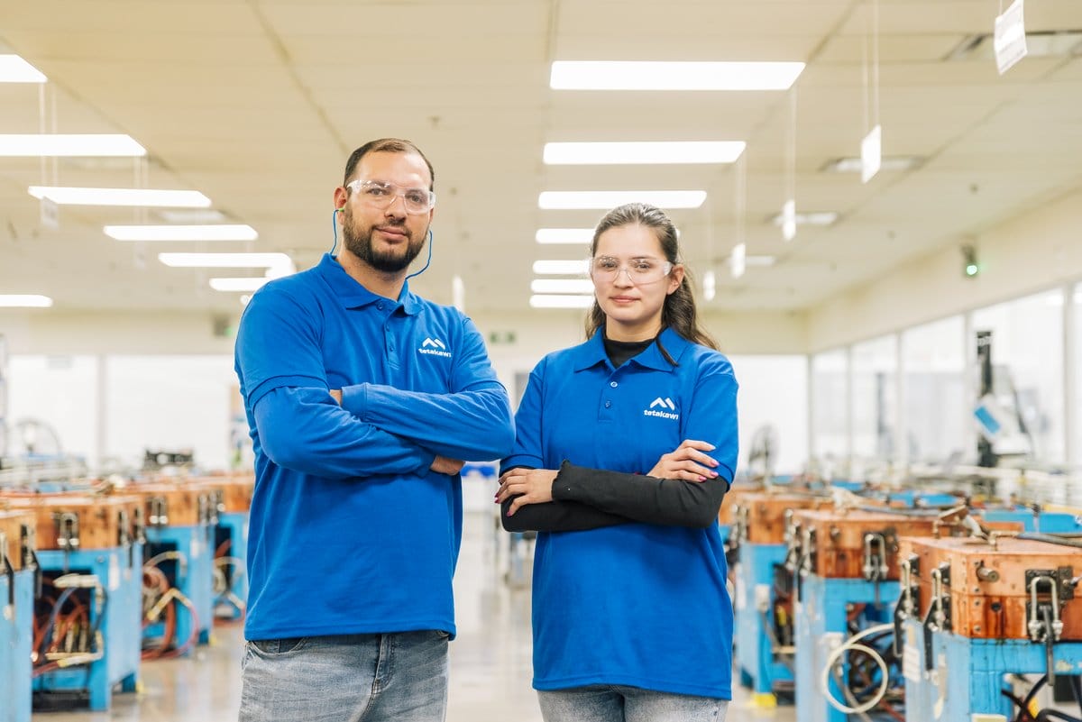 Two Tetakawi team members stand before automated welding equipment at a Manufacturing Campus in Mexico | Tetakawi