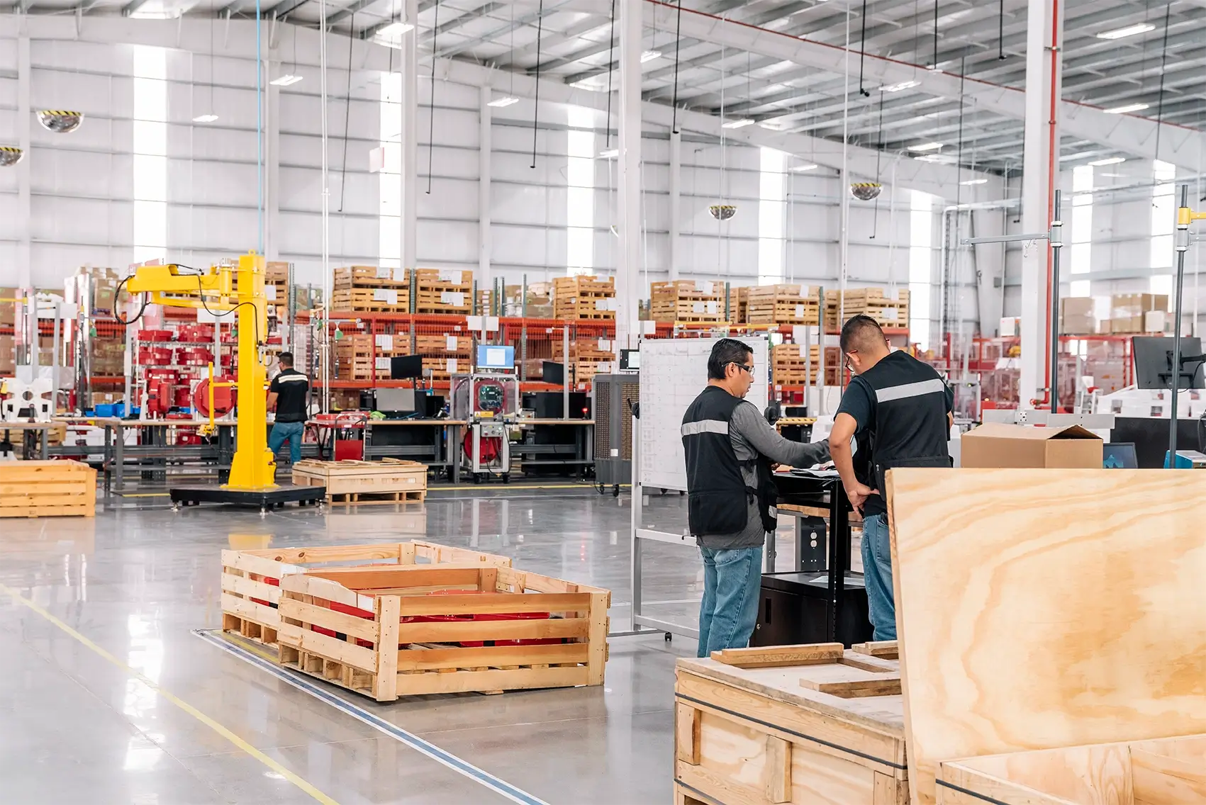 Two workers in safety vests reviewing documents at a workstation inside a large manufacturing building in Mexico | Tetakawi