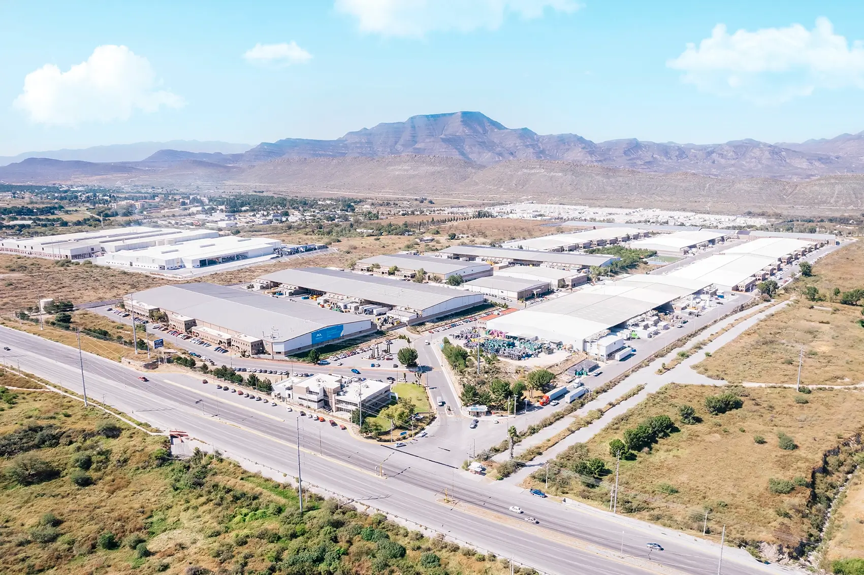 Aerial view of an industrial park with large manufacturing buildings beside a highway and mountains in Mexico | Tetakawi