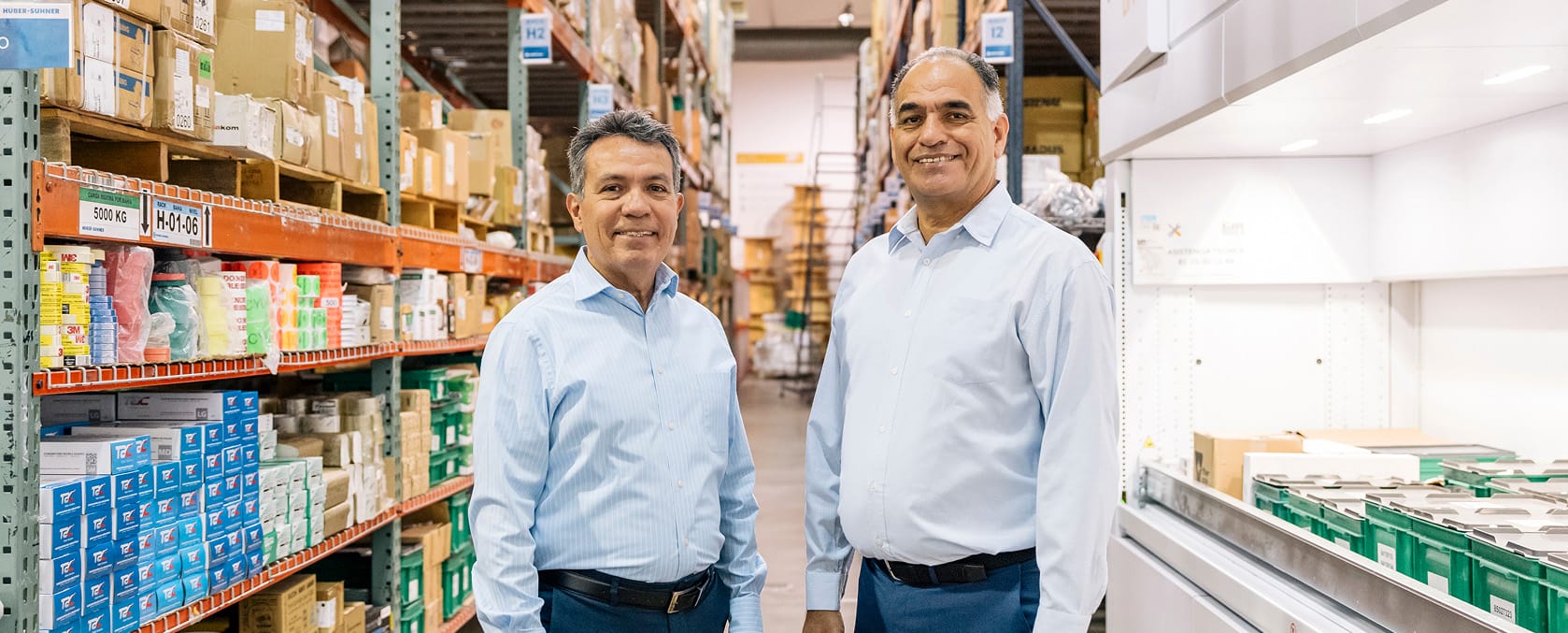 Two managers in light blue shirts standing between shelves of stocked supplies at a manufacturing site in Mexico | Tetakawi