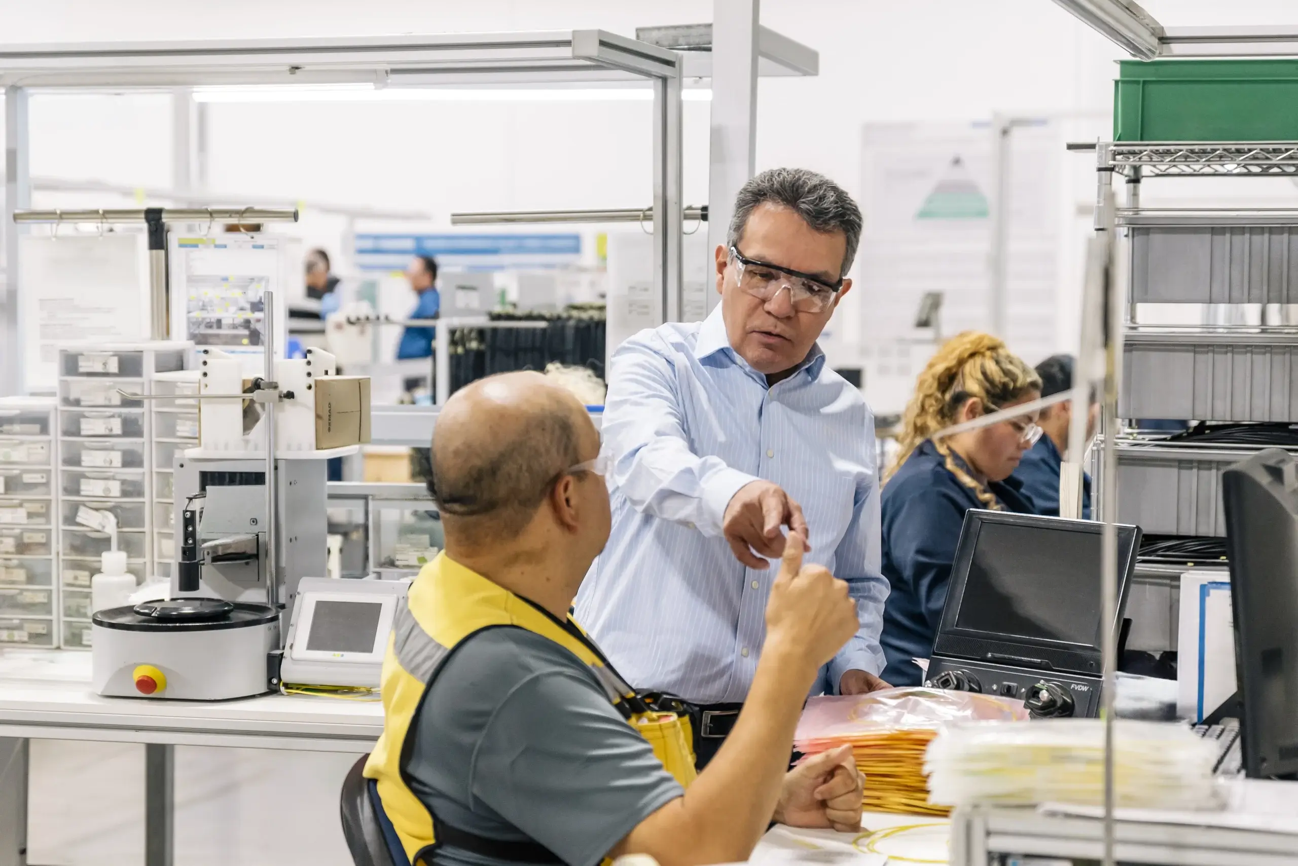 Manager in safety glasses talks with an operator at a HUBER+SUHNER assembly workstation in Empalme, Mexico | Tetakawi