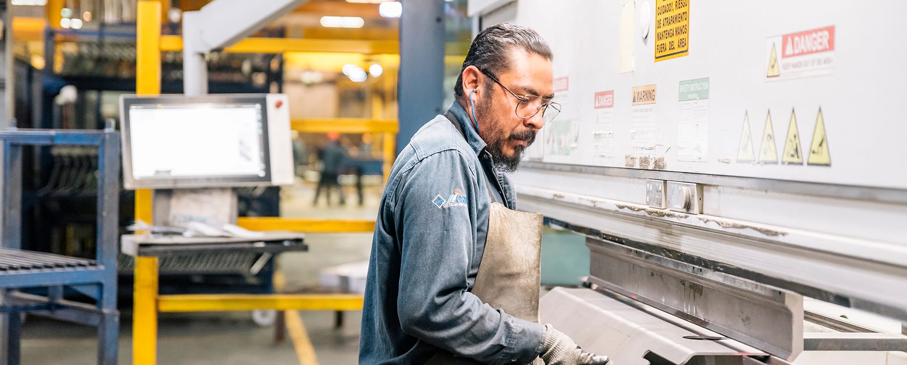 Press brake operator in safety glasses and a leather apron forming sheet metal, manufacturing in Mexico | Tetakawi