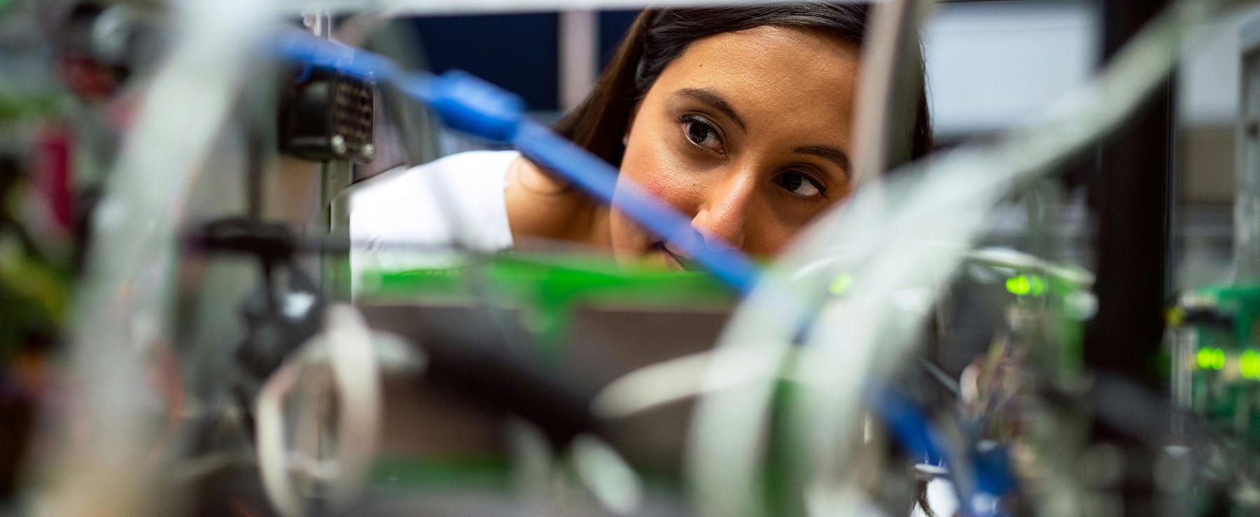 Engineer peering through wiring and electronic test equipment in a lab, representing manufacturing in Mexico | Tetakawi