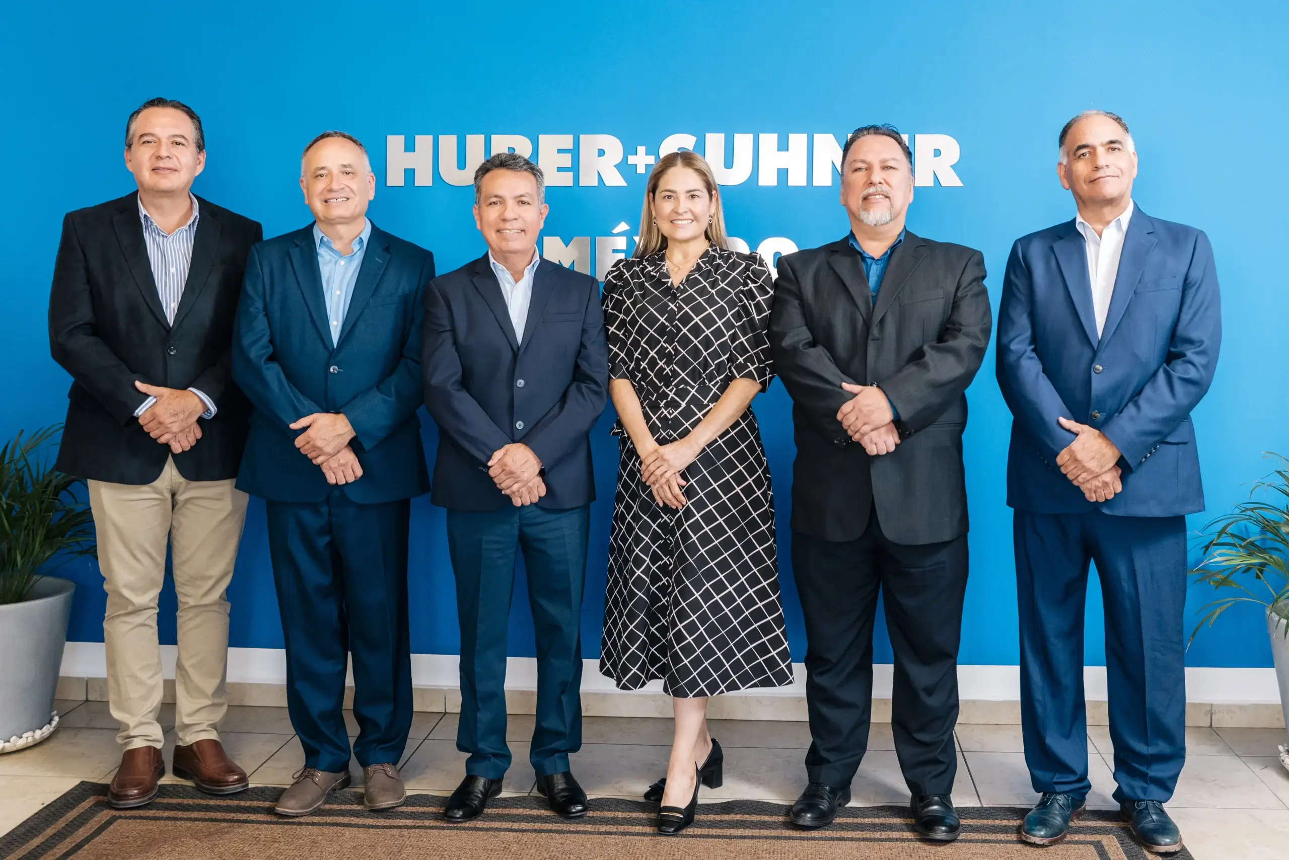 HUBER+SUHNER Mexico leadership team standing in front of the company's blue logo wall, manufacturing in Mexico | Tetakawi