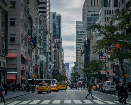 Downtown street with yellow taxis and US flags, representing US-based manufacturing compared with Mexico | Tetakawi