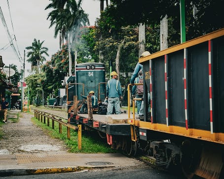 Rail workers in hard hats on a freight train in a palm-lined town, representing other nearshore options | Tetakawi