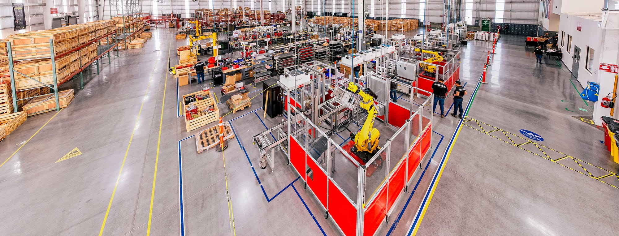 Wide view of a production floor with robotic work cells and wooden crates, manufacturing in Mexico | Tetakawi