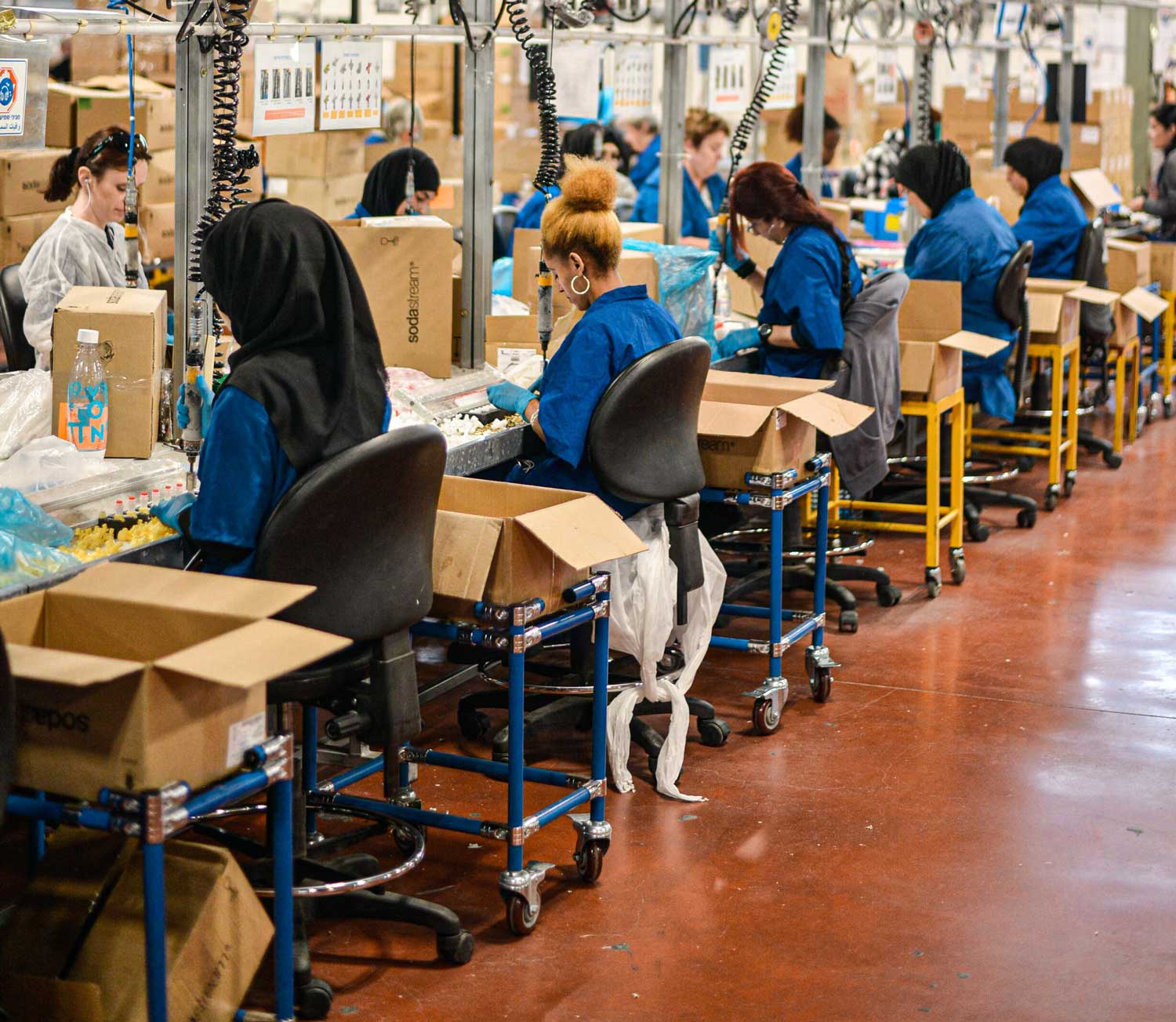 Assembly workers in blue smocks at production workstations, for a webinar on companies that offshore production | Tetakawi