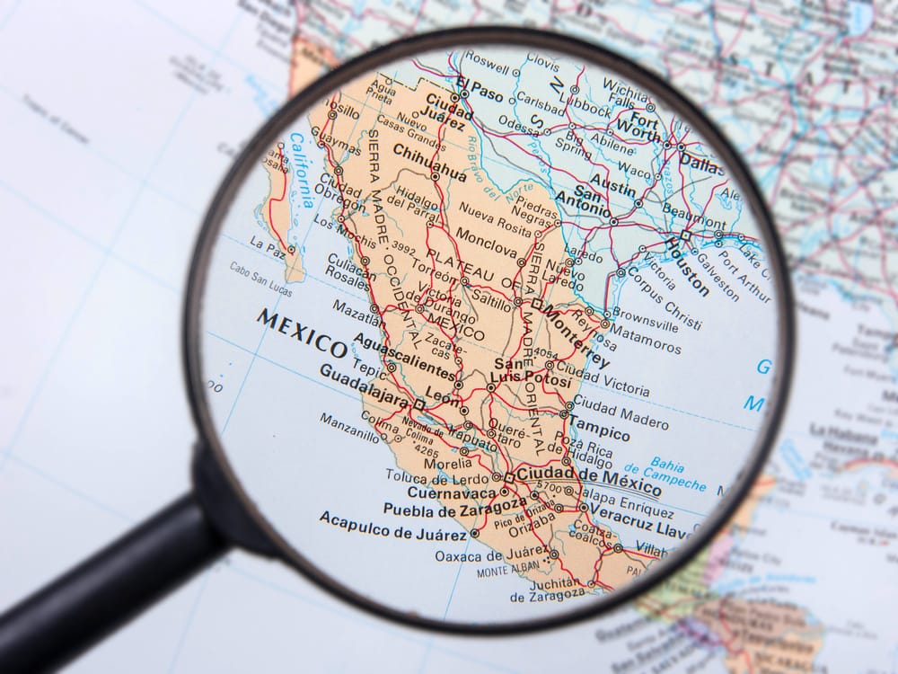 Magnifying glass over a printed map of Mexico, representing site selection for manufacturing in Mexico | Tetakawi