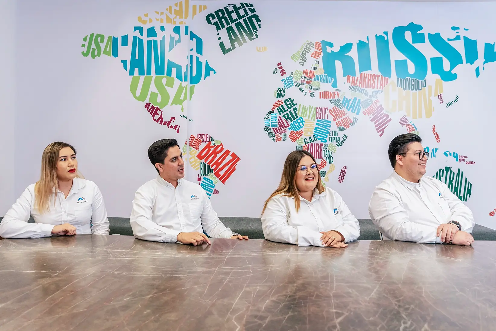 Four Tetakawi logistics team members seated at a table in front of a world map mural in their office in Mexico | Tetakawi