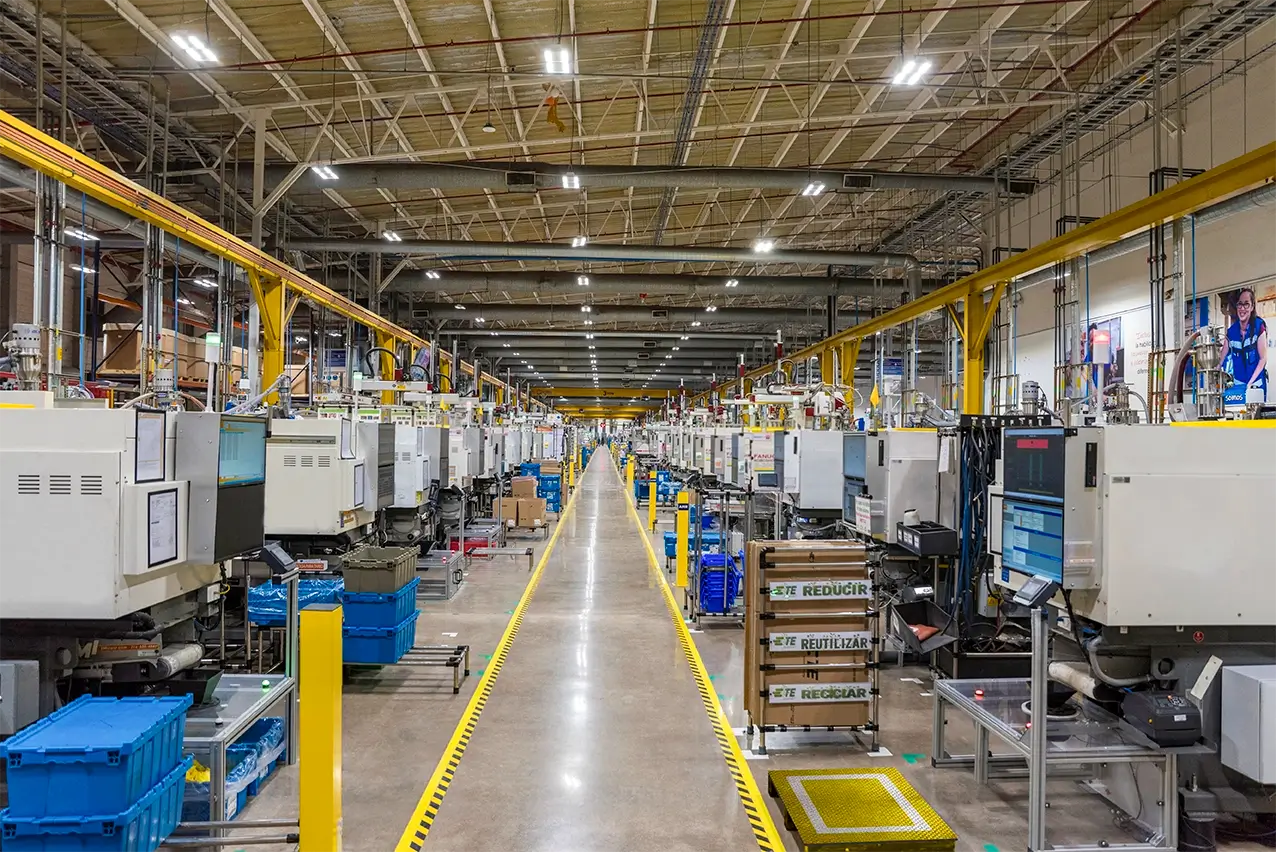 Rows of injection molding machines along a marked aisle with recycling bins on a manufacturing floor in Mexico | Tetakawi