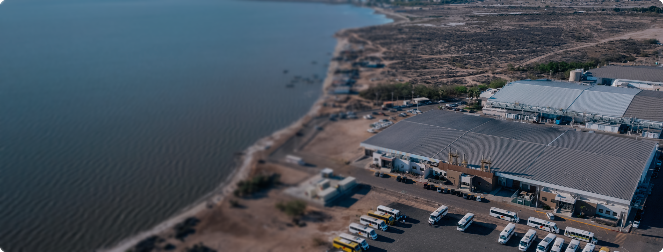 Aerial view of coastal manufacturing buildings with rows of buses parked outside, cost and workforce in Mexico | Tetakawi