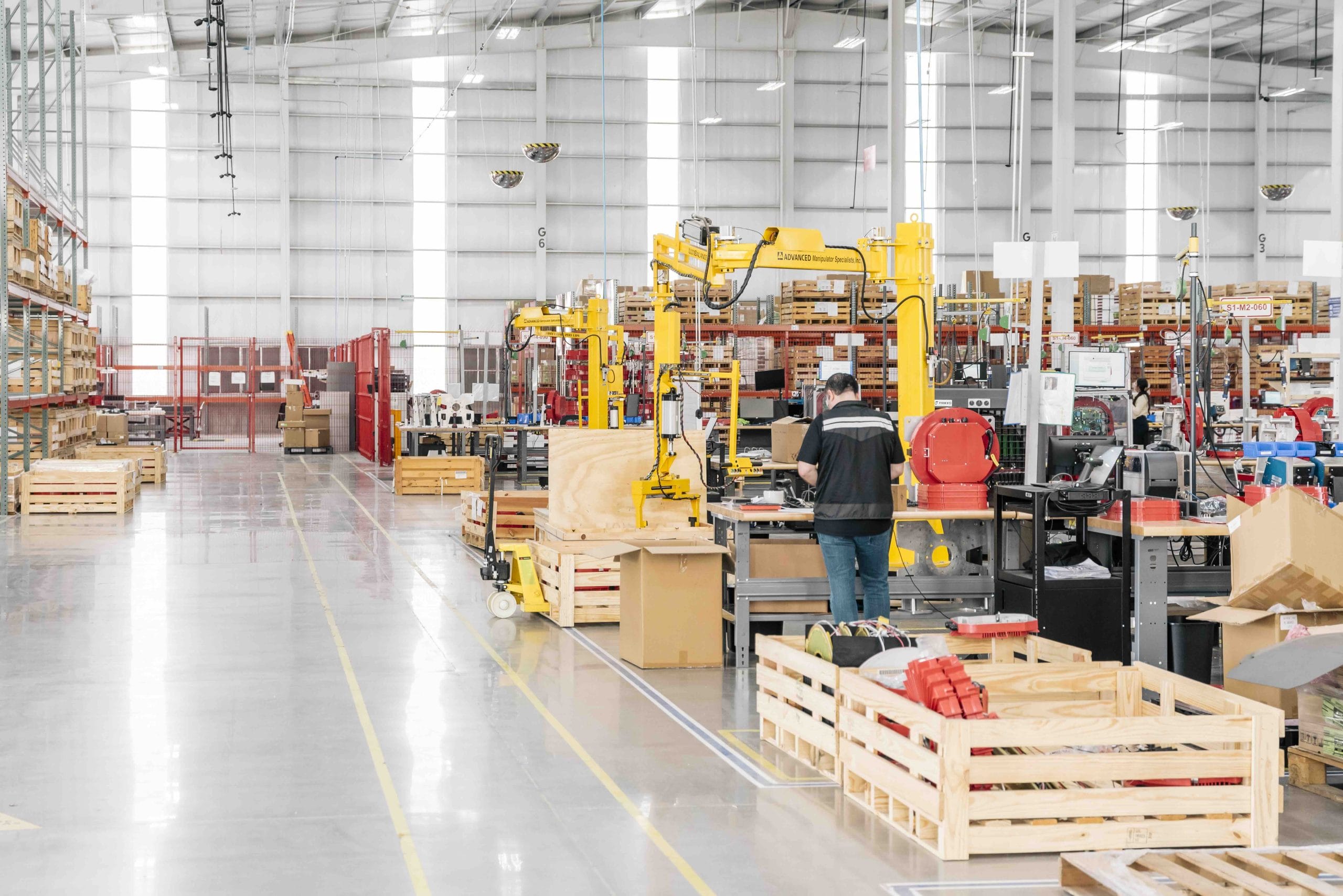 Operator at a workstation with yellow lift-assist arms and wooden crates on a bright production floor in Mexico | Tetakawi