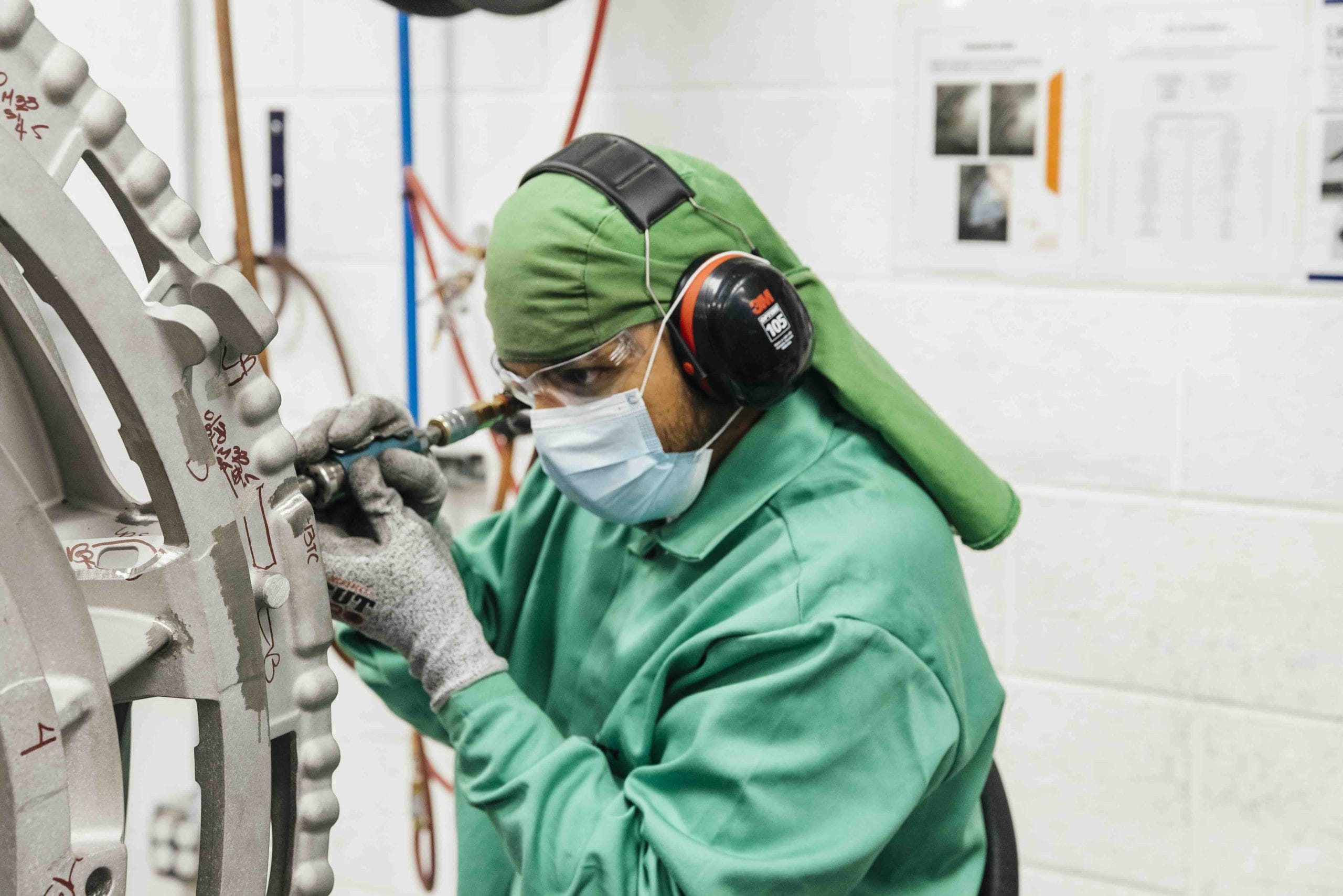 CPP worker in protective hood, ear muffs and mask grinding a large aerospace metal casting in Mexico | Tetakawi