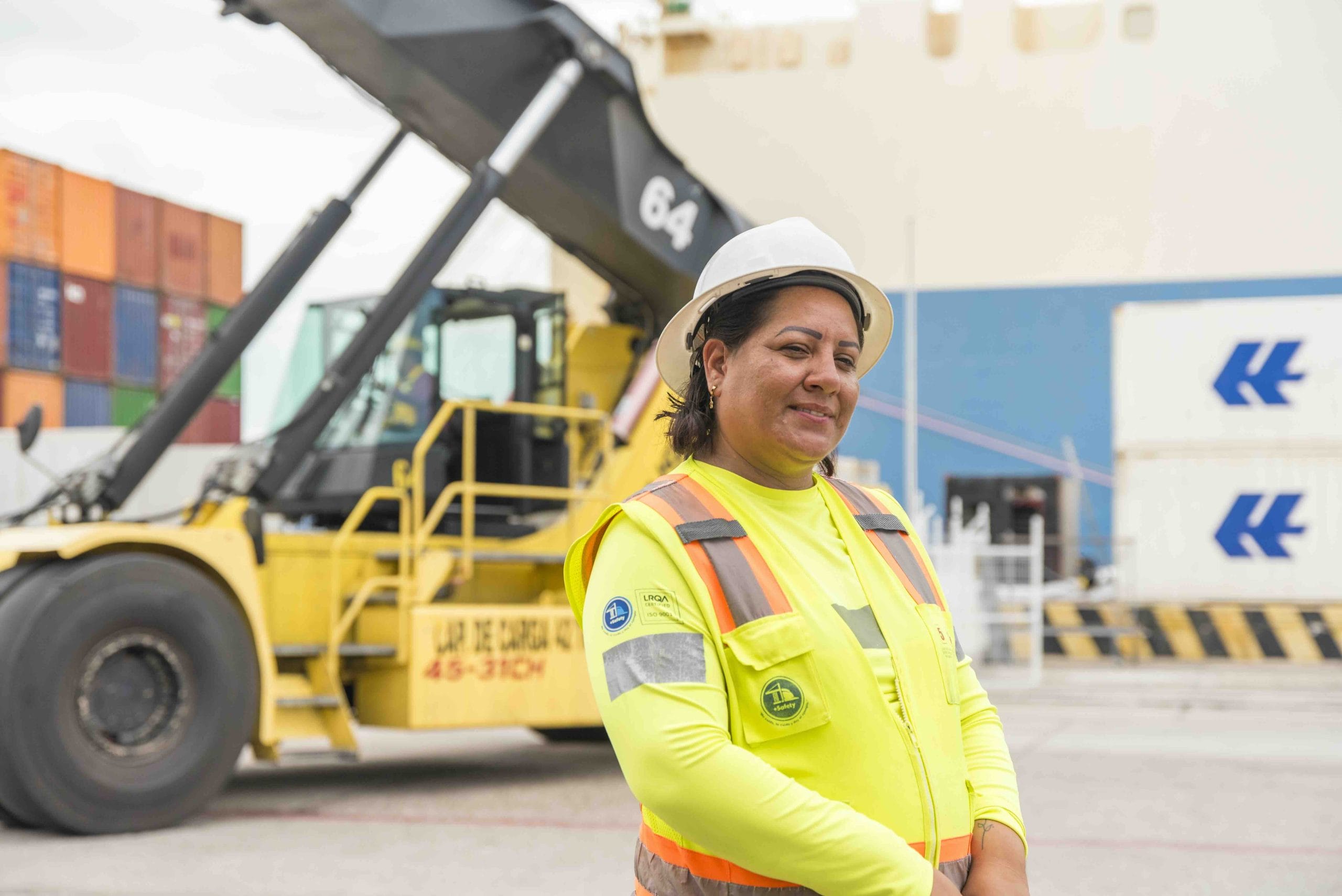 Logistics worker in a hard hat and safety vest beside a container reach stacker at a port in Mazatlán, Mexico | Tetakawi