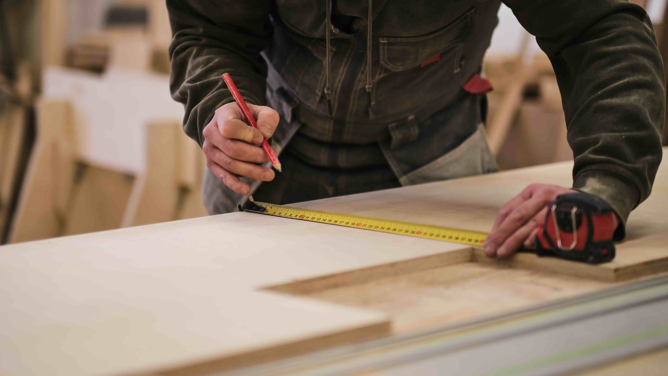 Carpenter marking a plywood panel with a tape measure and pencil, showing furniture manufacturing in Mexico | Tetakawi