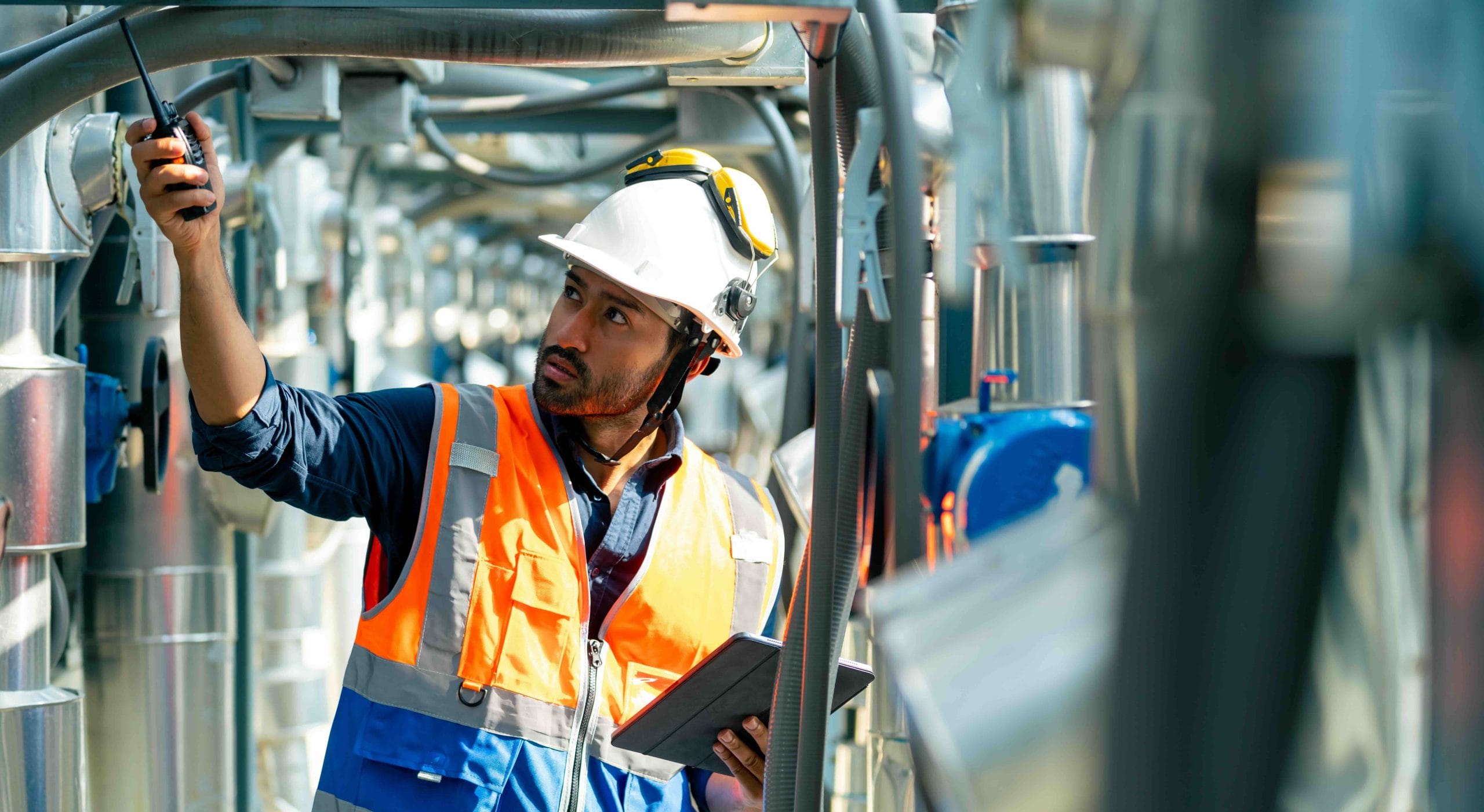 Engineer in a hard hat and safety vest inspecting industrial ductwork with a tablet, HVAC manufacturing in Mexico | Tetakawi
