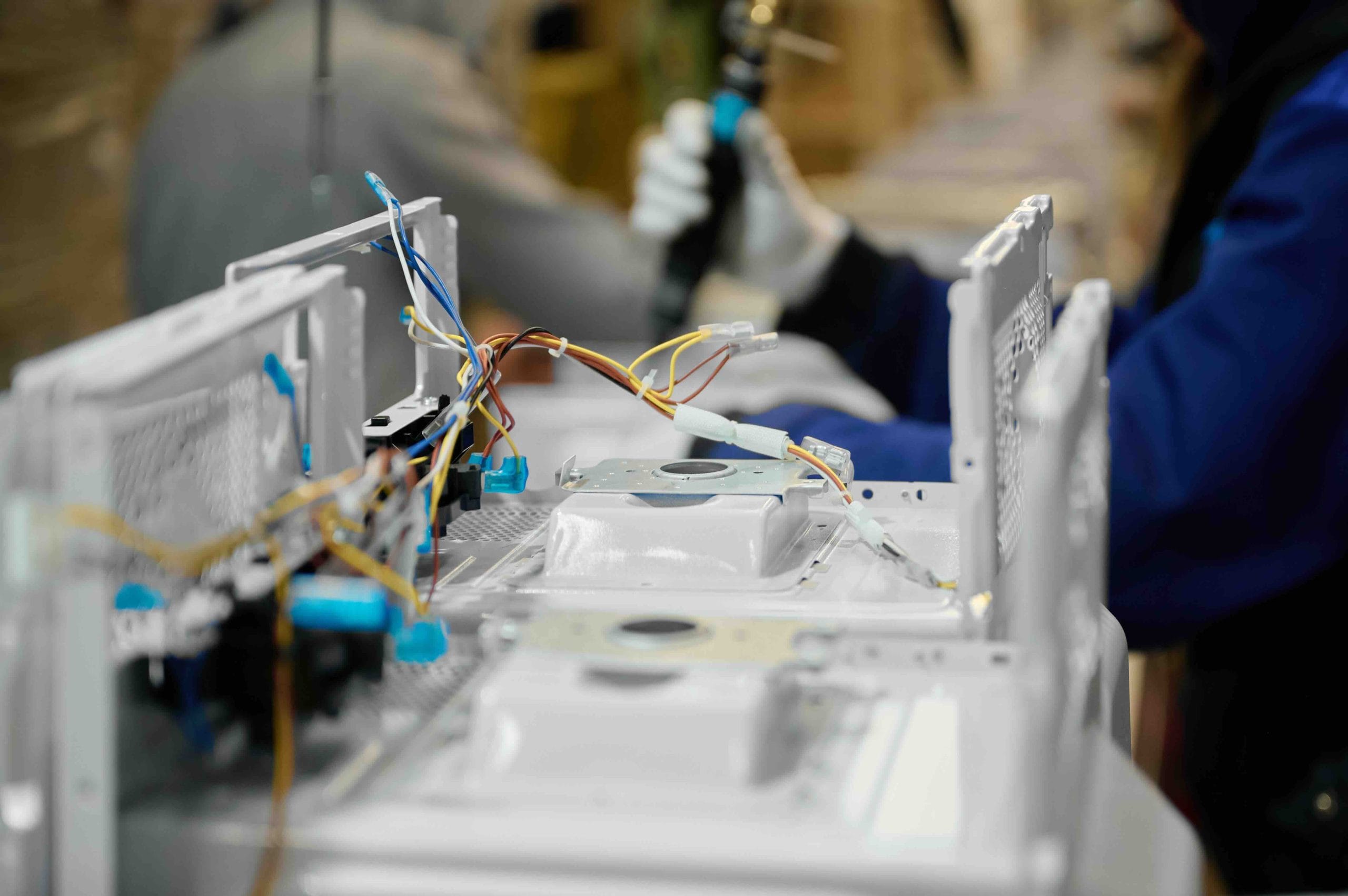 Gloved worker wiring white appliance chassis on an assembly line, showing skilled manufacturing labor in Mexico | Tetakawi