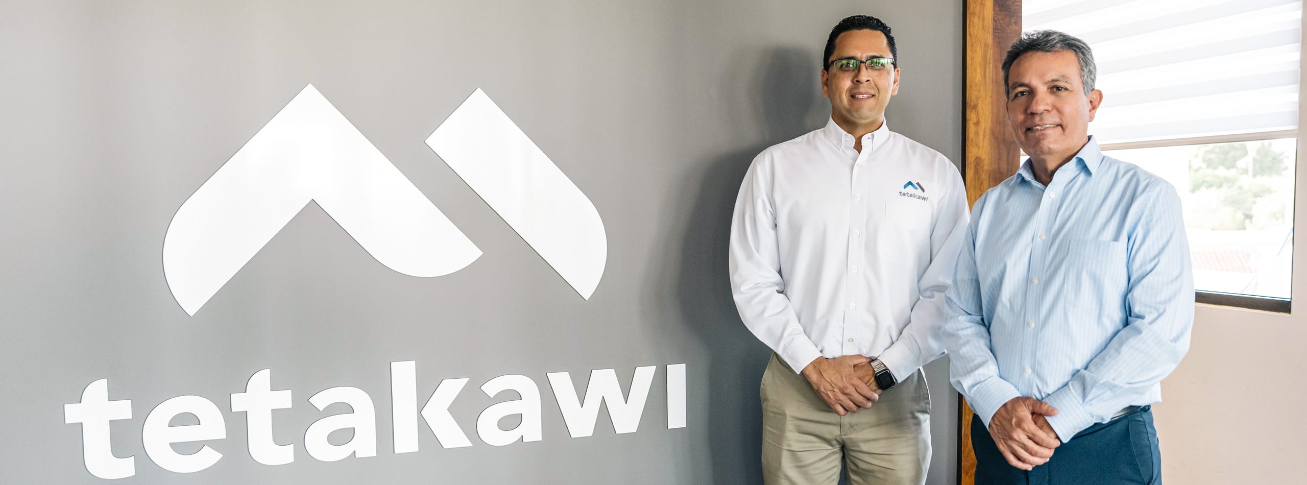 Tetakawi team member and a colleague standing beside the Tetakawi logo wall, supporting workforce needs in Mexico | Tetakawi