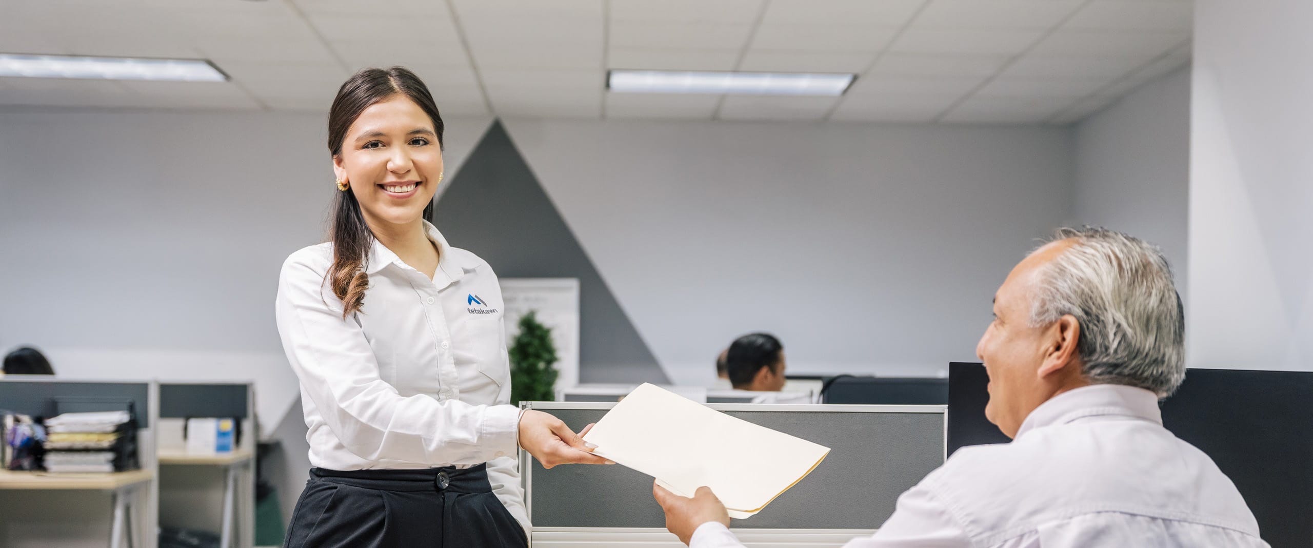 Tetakawi team member handing documents to a colleague in a Mexico office, representing fiscal and tax compliance support