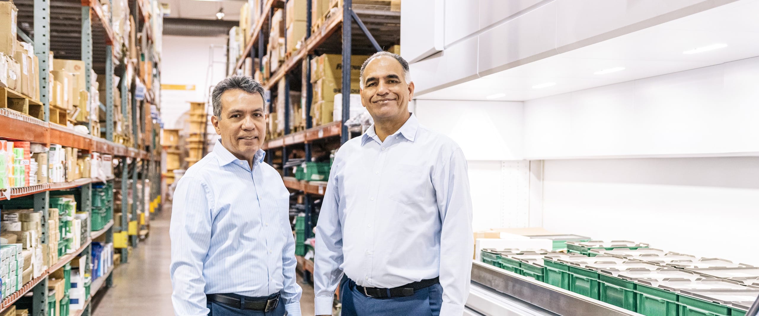 Two managers standing between shelves of stocked supplies at a manufacturing site in Mexico