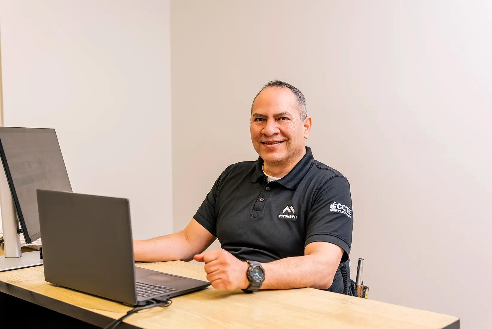 Smiling Tetakawi team member in a black branded polo working on a laptop at a desk, inclusive training in Mexico | Tetakawi