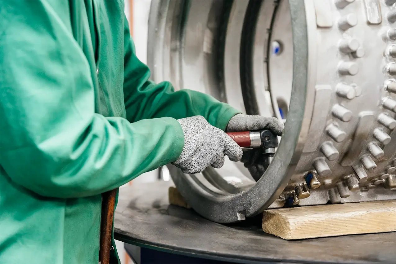 Operator in green coveralls and cut-resistant gloves working on a large flange, manufacturing in Mexico | Tetakawi