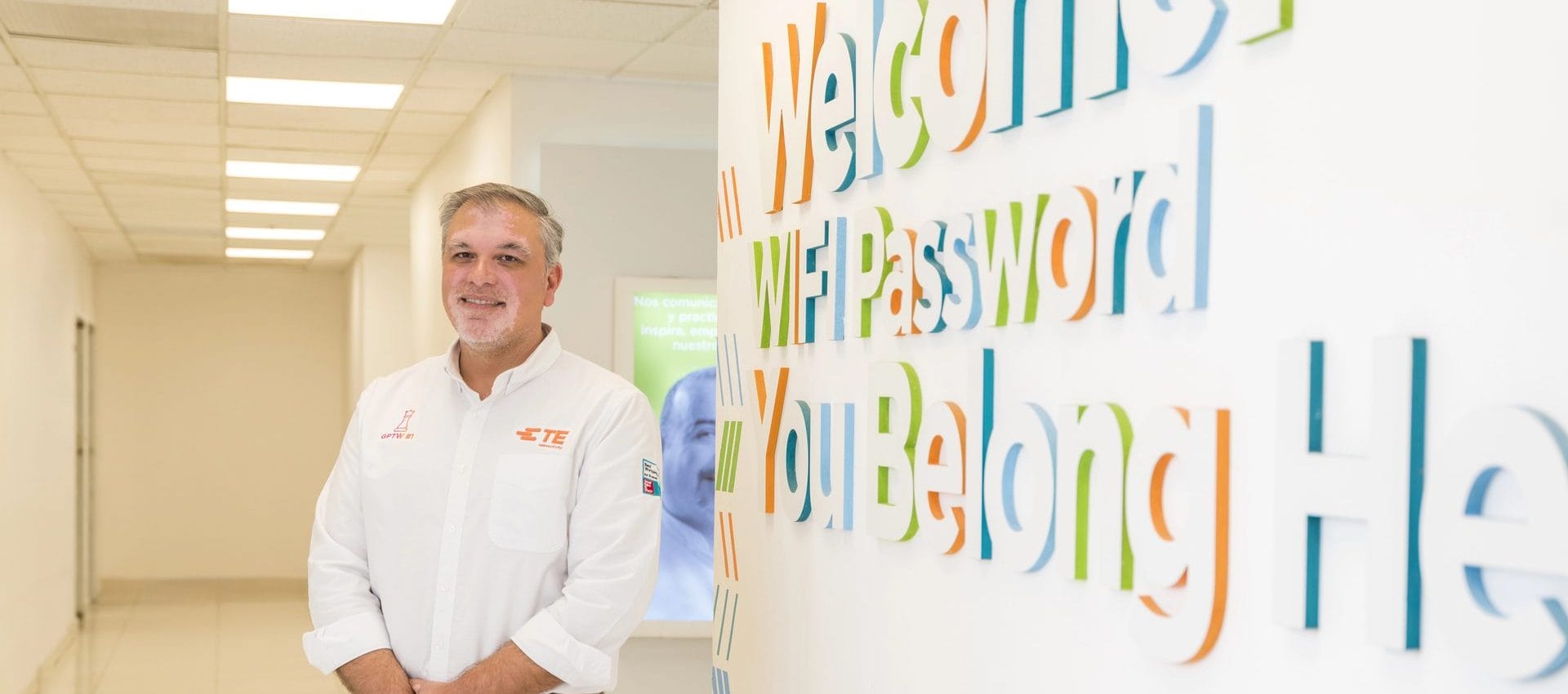 TE Connectivity team member beside a colorful You Belong Here welcome wall at the plant in Empalme, Mexico | Tetakawi