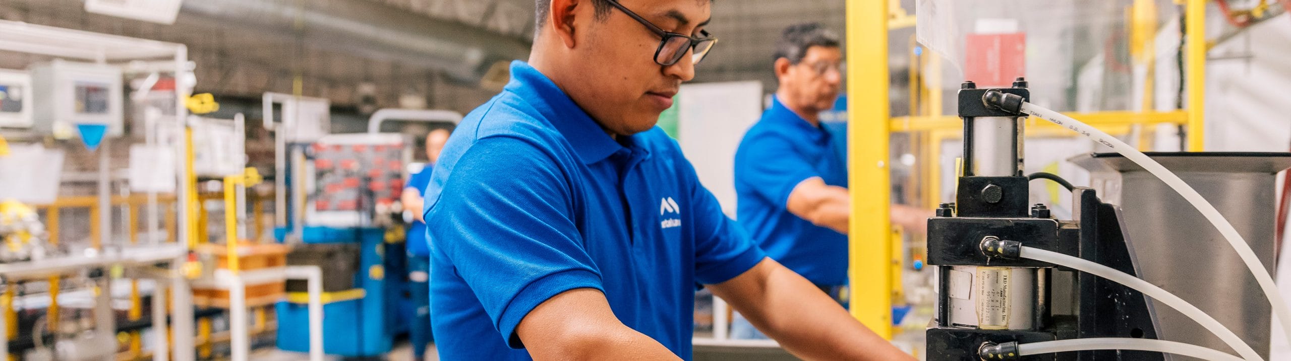 Technicians in blue Tetakawi polos operate pneumatic production equipment on an automotive line in Mexico | Tetakawi