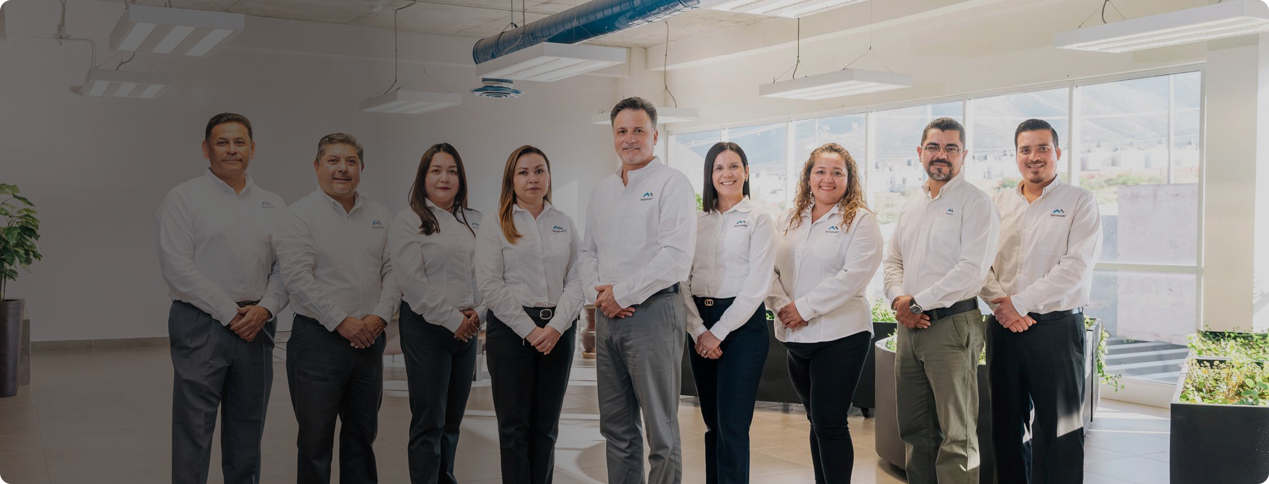 Tetakawi leadership team in white company shirts standing together in a bright office in Saltillo, Mexico | Tetakawi