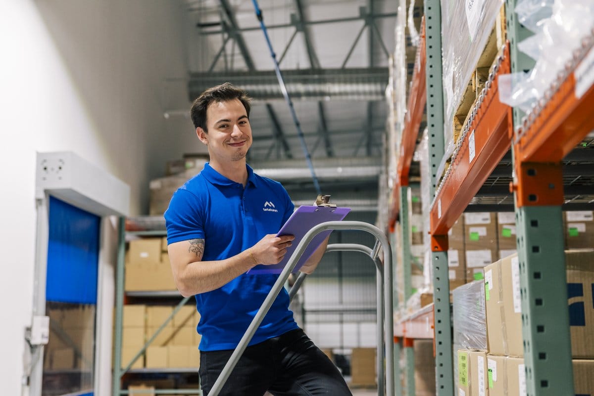 Tetakawi team member on a rolling ladder with a clipboard auditing inventory racks for compliance in Mexico | Tetakawi