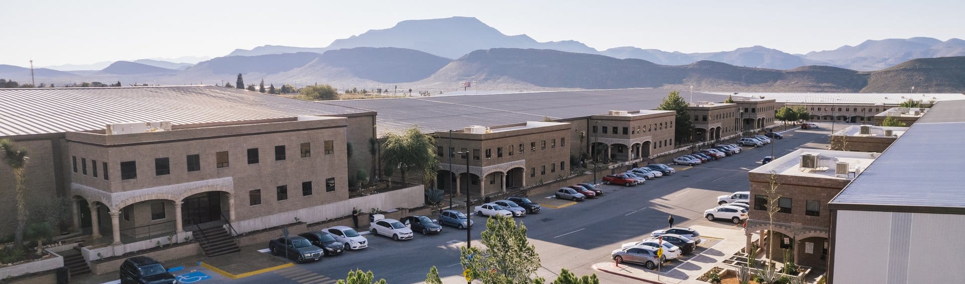 Aerial view of a Tetakawi Manufacturing Campus in Mexico, showing office buildings, parking, and the surrounding mountain landscape