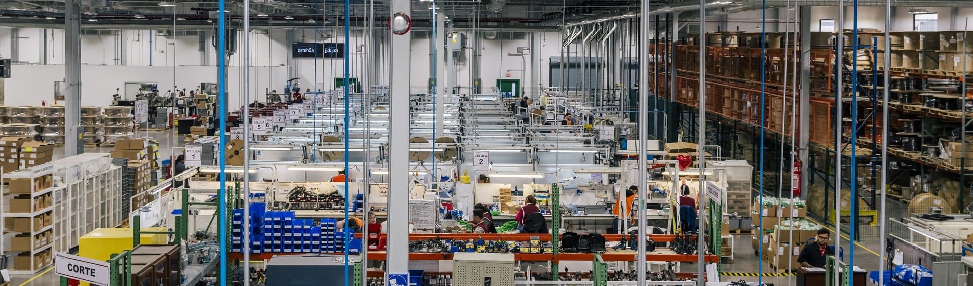 Wide view of a Tetakawi Manufacturing Campus production floor in Mexico, showing organized work cells, staff, and warehouse racking