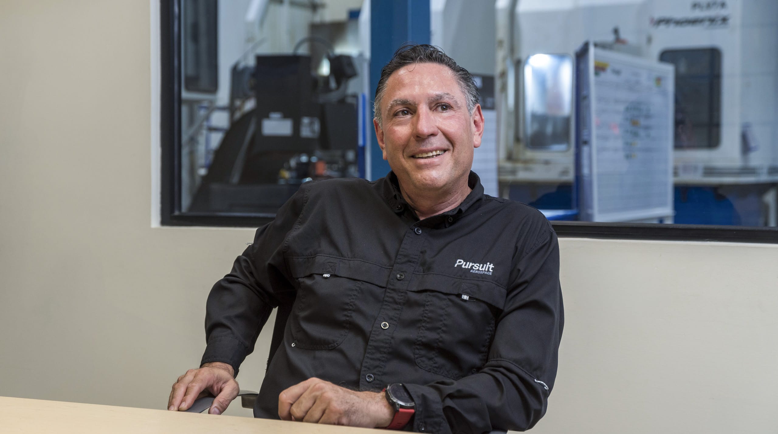 Pursuit Aerospace general manager smiling in front of CNC machining equipment at Tetakawi's Roca Fuerte Campus in Guaymas, Mexico