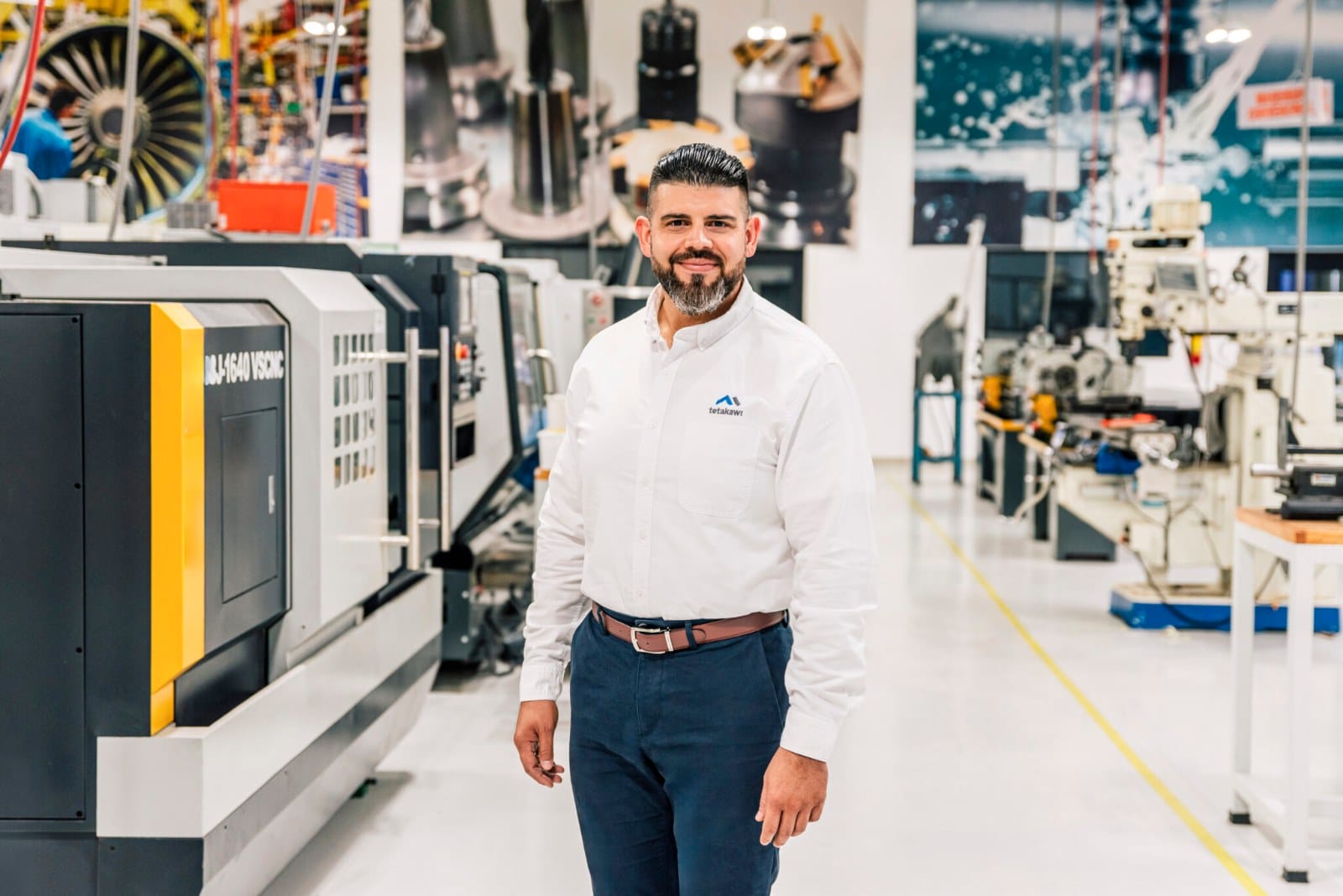 Tetakawi team member in a branded white shirt standing among CNC machines in a machining area in Mexico | Tetakawi
