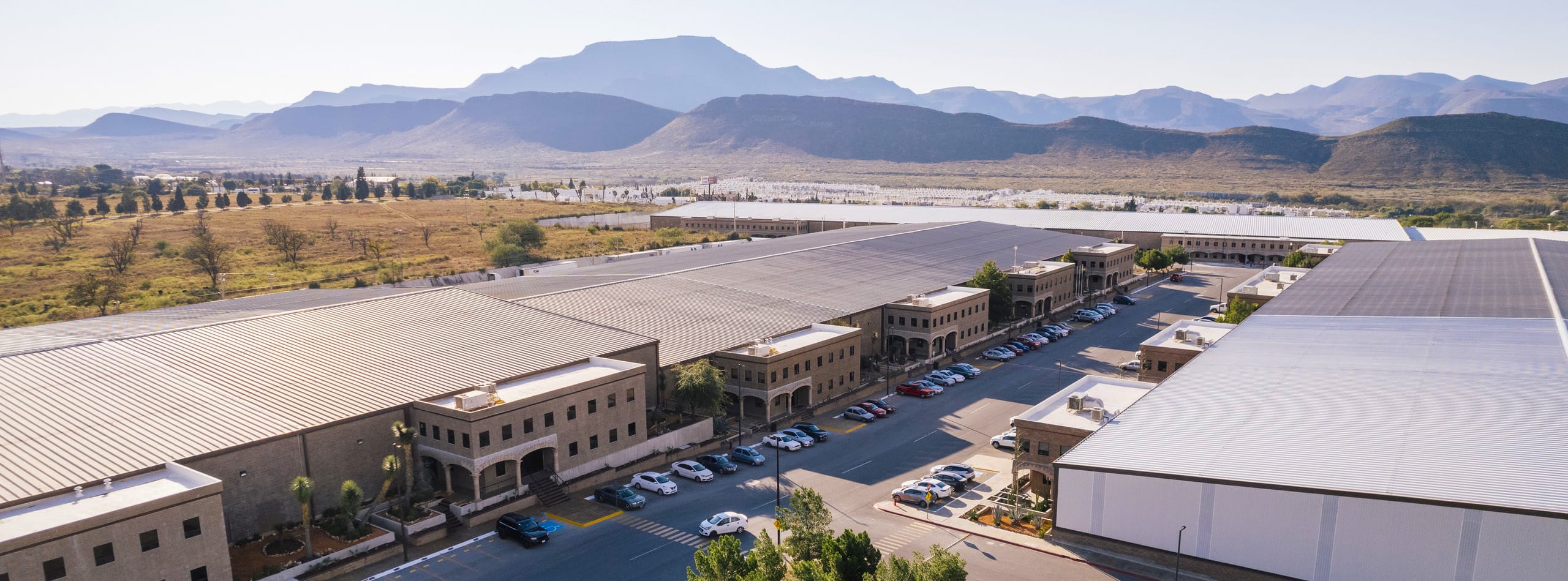 Aerial view of a Tetakawi Manufacturing Campus in Mexico, showing office buildings, parking, and the surrounding mountain landscape